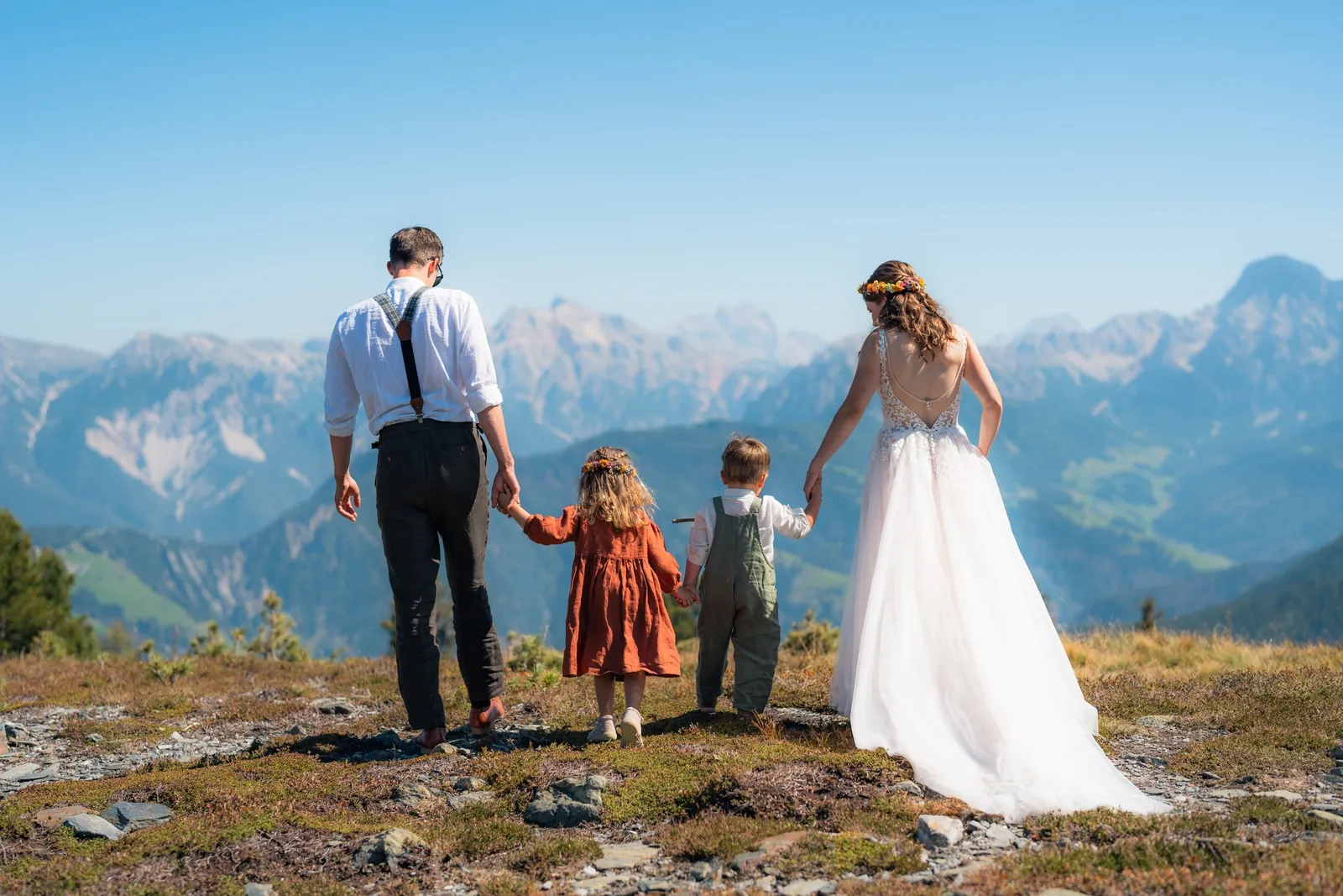 Brautpaar mit Kindern blickt von der Alm auf die Dolomiten