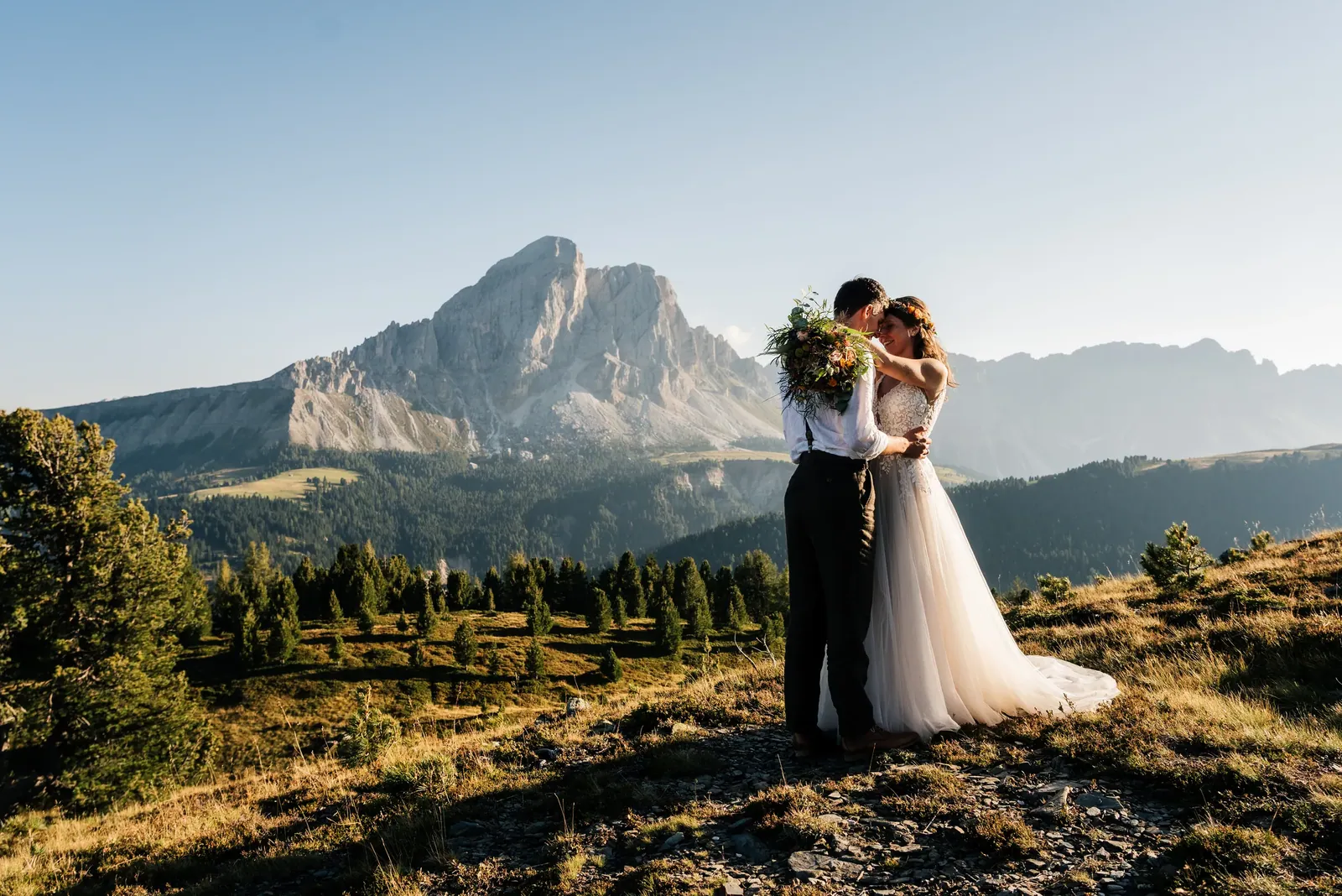 Brautpaar umarmt sich auf der Almwiese vor dem Dolomitengipfel