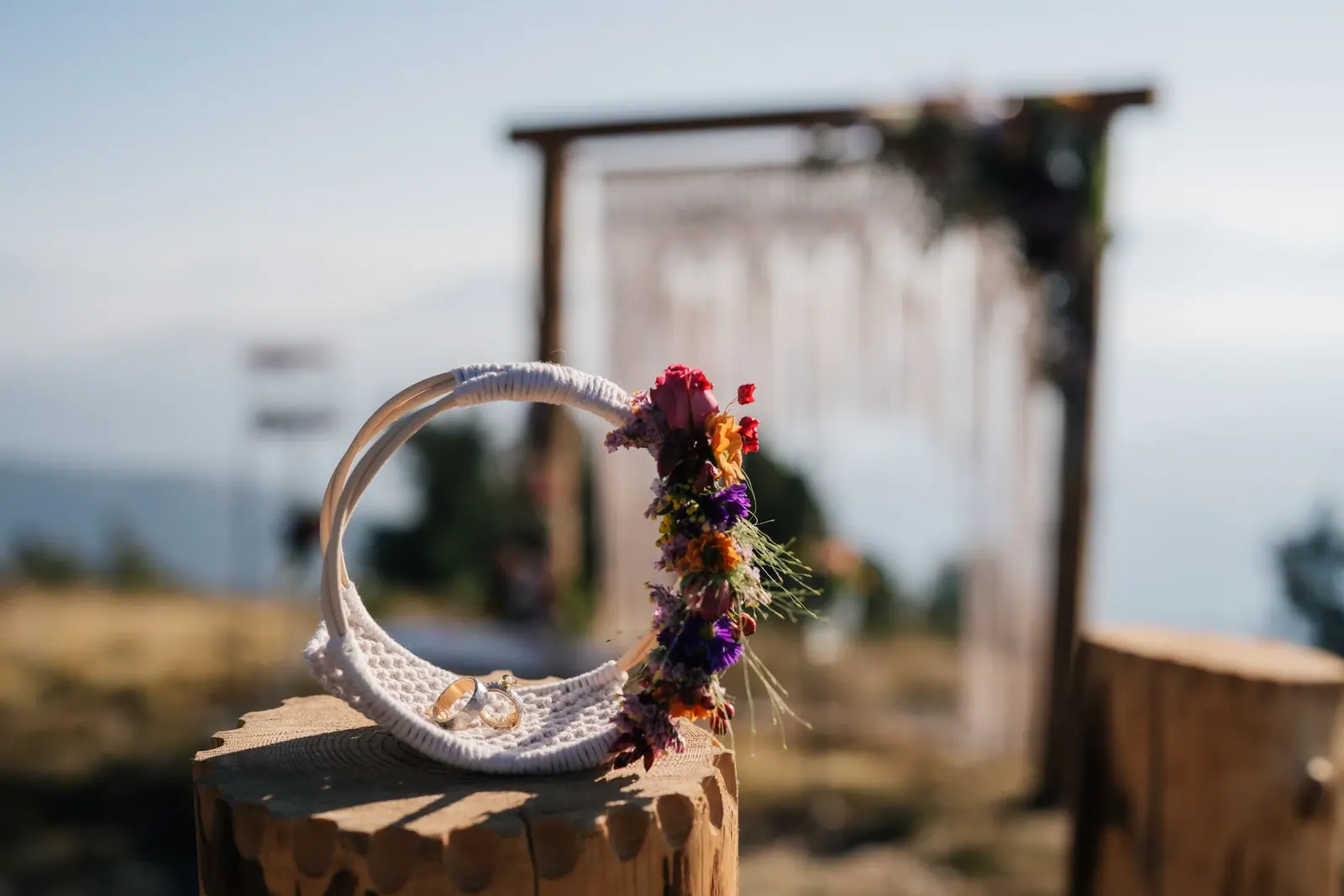 Eheringe in einem Makramee-Ring mit Blumen vor dem Traubogen auf dem Berg