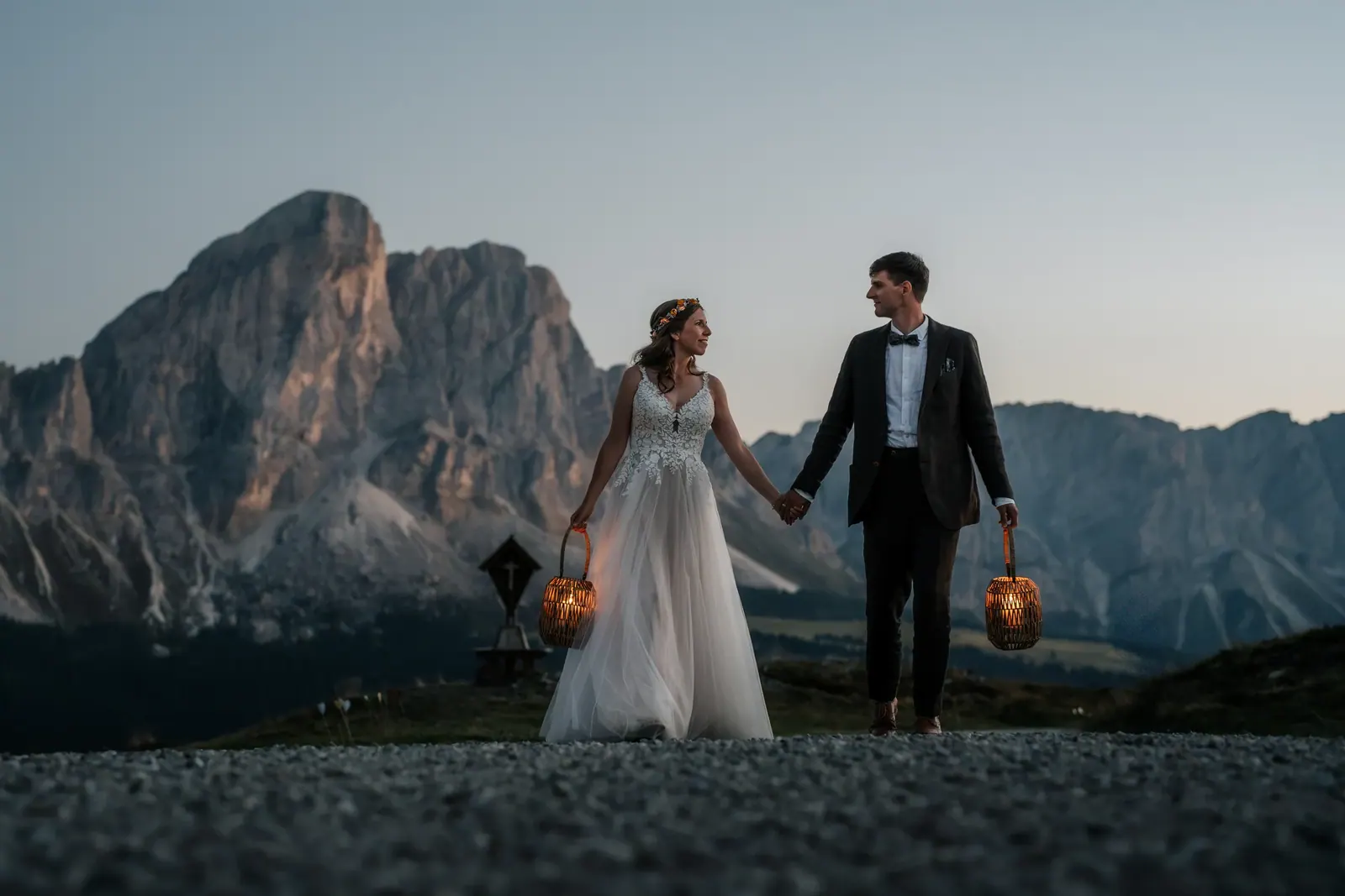 Brautpaar geht mit leuchtenden Laternen Hand in Hand vor dem Dolomitengipfel in der Dämmerung