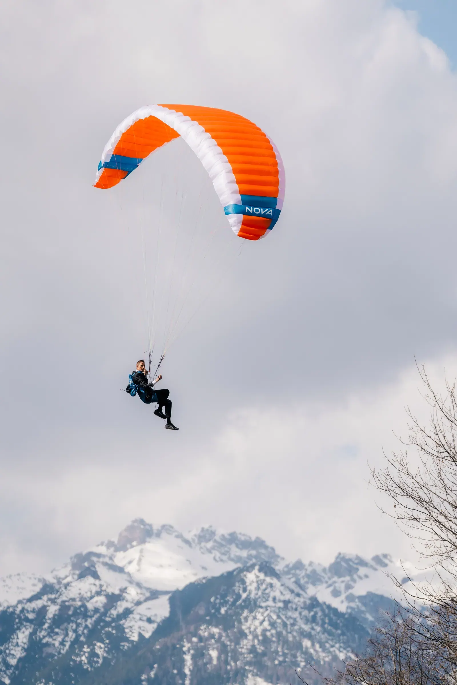Bräutigam fliegt mit dem Gleitschirm vor verschneiten Gipfeln zum Standesamt