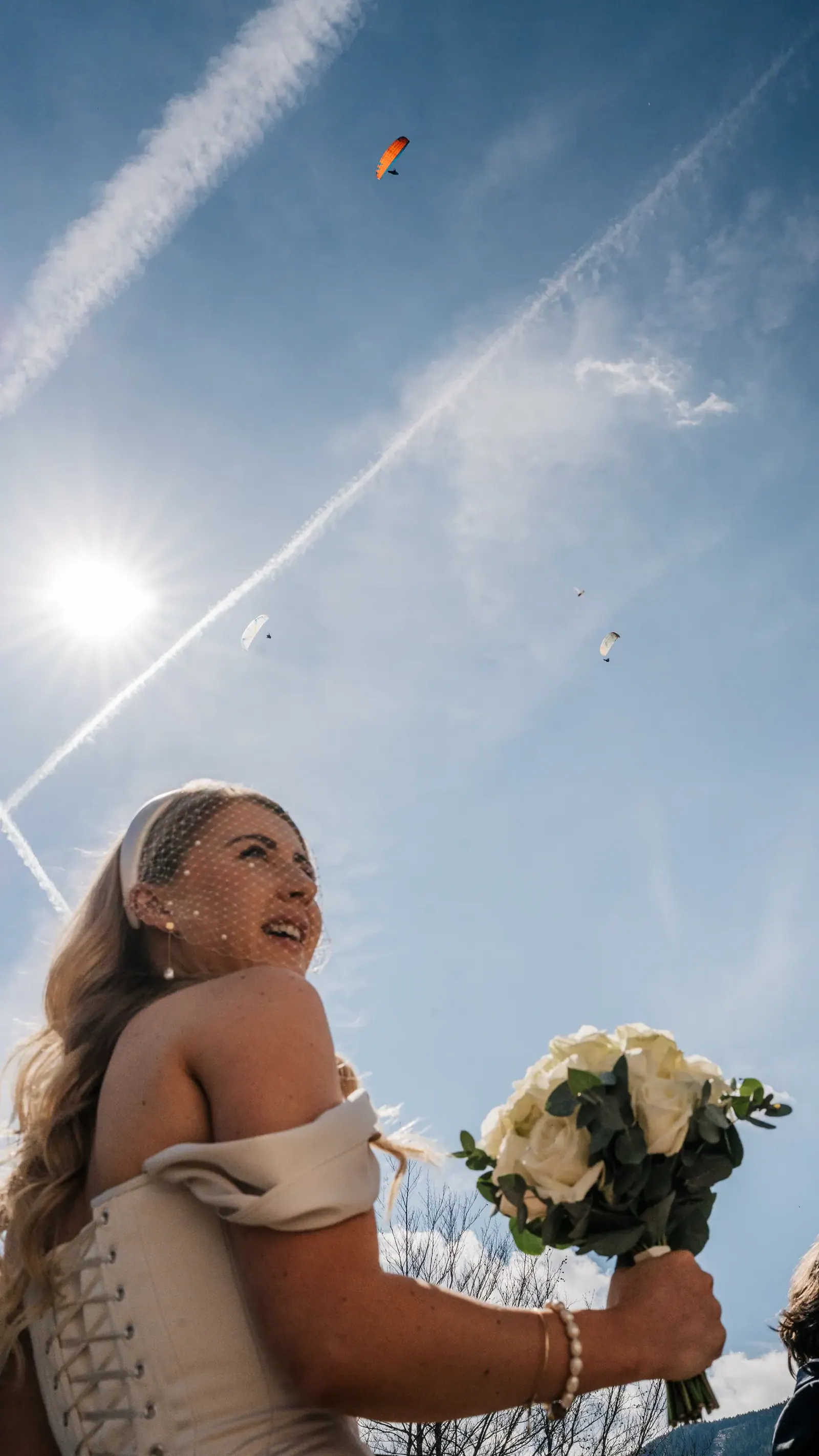 Braut blickt lachend in den Himmel zu den Gleitschirmen