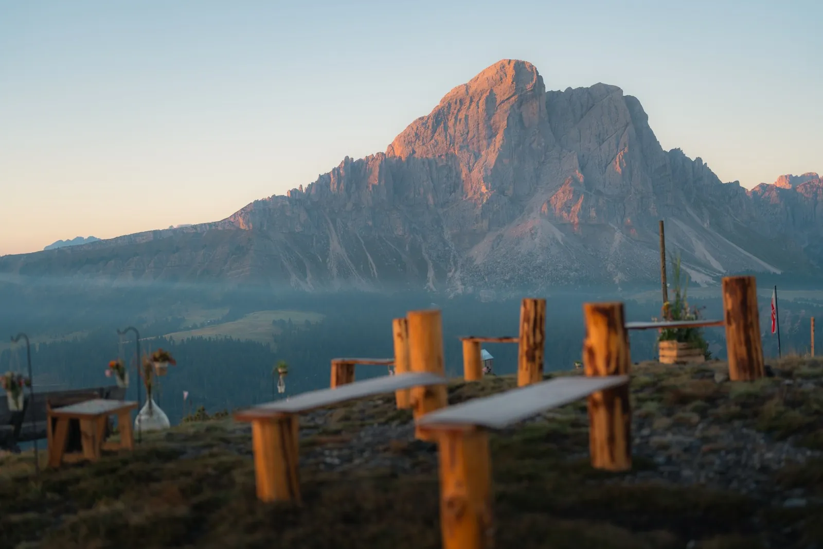 Holzbänke am Trauungsplatz auf der Alm, dahinter der Dolomitengipfel im Morgenlicht
